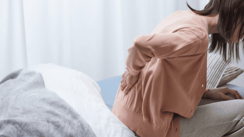 布団から起きてせなかを抑える女性