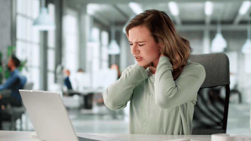 パソコン仕事をしながら首を抑える女性