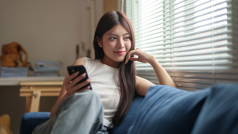 スマホを持ちながら窓の外を見る女性